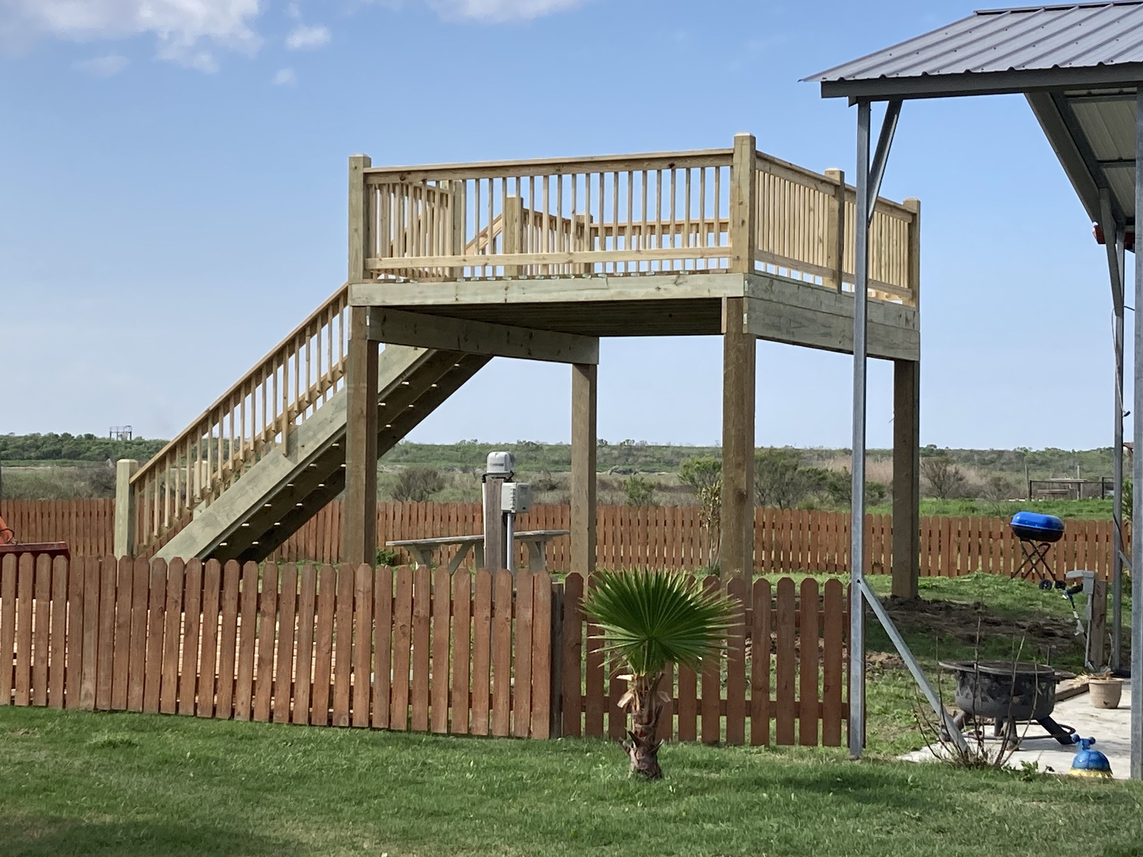 Een houten terras met een trap naar een platform, omringd door een houten hek en een palmboom.