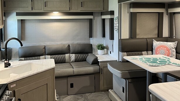 A compact RV interior with a kitchenette, seating area, and a small table. - Beautiful NEW 2023 camper covered on concrete slab. Sit and enjoy the barges (Bolivar Peninsula)