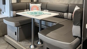 A compact RV interior with a dining area, seating, and storage compartments. - Beautiful NEW 2023 camper covered on concrete slab. Sit and enjoy the barges (Bolivar Peninsula)
