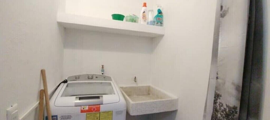 A small bathroom with a washing machine, a sink, and a shelf above the sink holding toiletries.