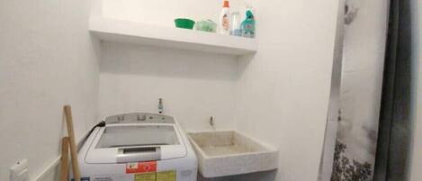 A small bathroom with a washing machine, a sink, and a shelf above the sink holding toiletries.