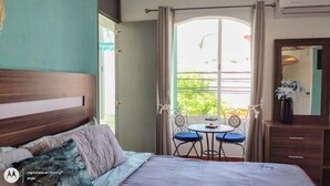 A hotel room with a bed, a small table with two chairs, a window with curtains, and a dresser.