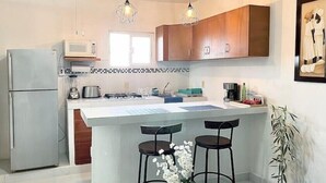 A modern kitchen with a central island, bar stools, a refrigerator, and a microwave.