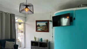 A living room with a teal accent wall, a TV mounted on it, a dark blue sofa, a glass cabinet, and a pendant light.