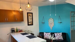 A compact living space with a kitchen area, a dining table, a sofa, and decorative wall hangings.