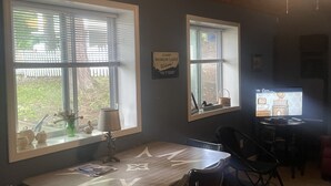 A dining area with a table and chairs, two windows with blinds, a lamp, and a sign on the wall. - #8 cottage comes with boat docks and shares over 600’ of frontage on Hamlin lake (Ludington)