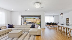 Un salon moderne avec un canapé d’angle, un coin repas doté de tabourets de bar et une cuisine avec un bar.