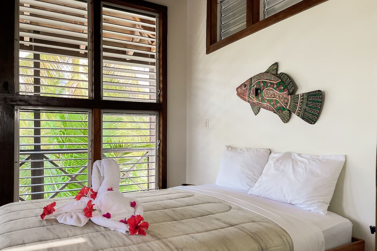 Une chambre à coucher avec un lit, des oreillers blancs et un poisson décoratif accroché au mur.