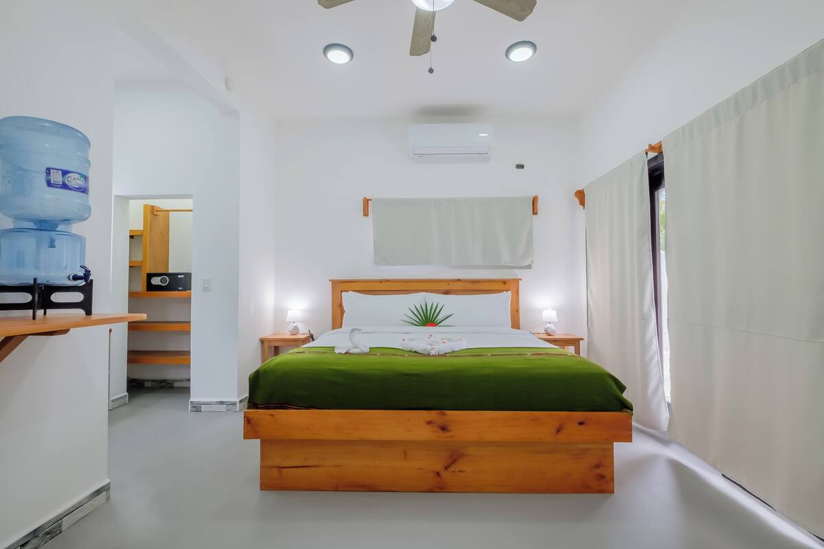 Une chambre avec un lit en bois, une literie verte, un distributeur d’eau et un ventilateur de plafond.