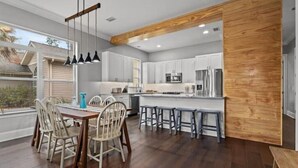 Une cuisine moderne avec des armoires blanches, un mur d’accent en bois et un coin repas comprenant une table et des chaises en bois.