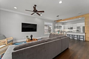 Un salon moderne avec un canapé d’angle gris, un téléviseur à écran plat fixé au mur, un ventilateur de plafond et un mur décoratif en bois.