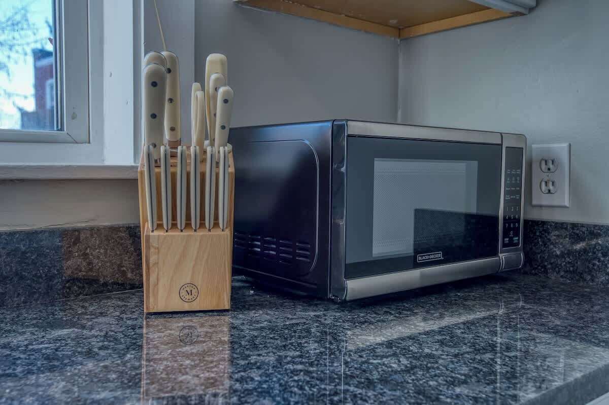 Un horno microondas sobre una encimera de granito junto a un bloque de cuchillos de madera.