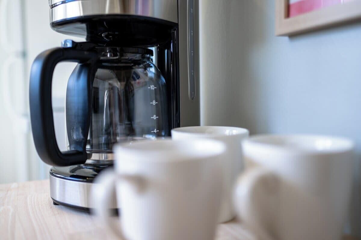 A coffee maker with a clear glass carafe and a black handle, placed on a wooden surface.
