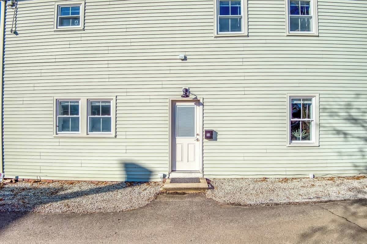 A light-colored two-story house with a central door, two windows on each floor, and a small porch.