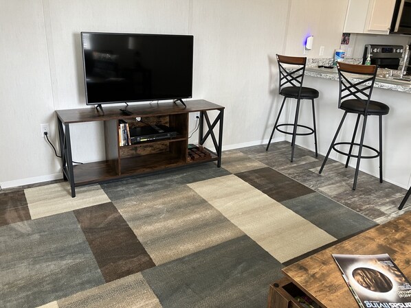 A living room with a TV on a wooden stand, two bar stools, a coffee table, and a rug. - Just minutes from Hill Creek Park and marina with room for your boat. (Edgemont)