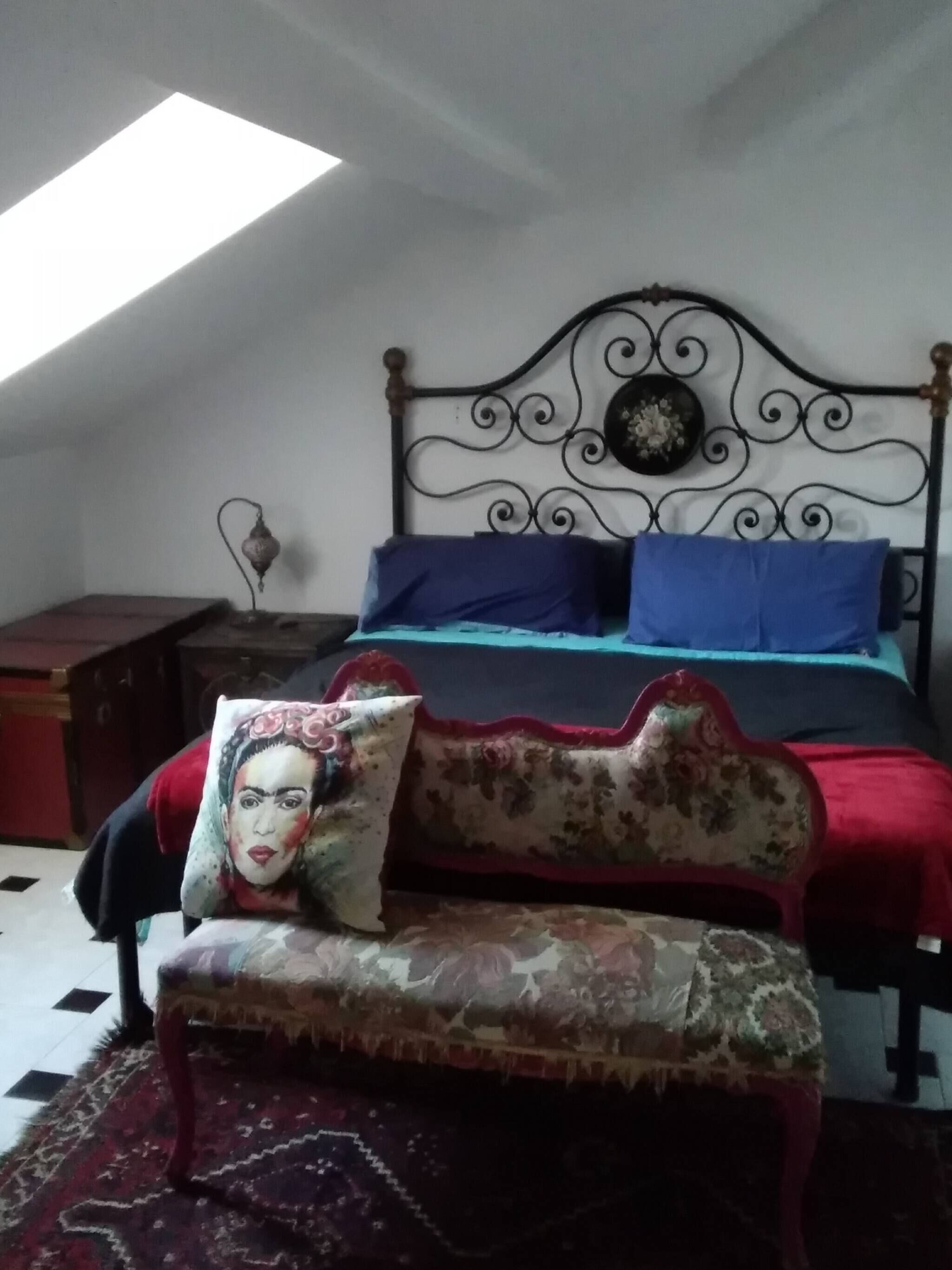 Ein Schlafzimmer mit Bett, Sitzbank, Nachttisch, Wanduhr und Dachfenster.