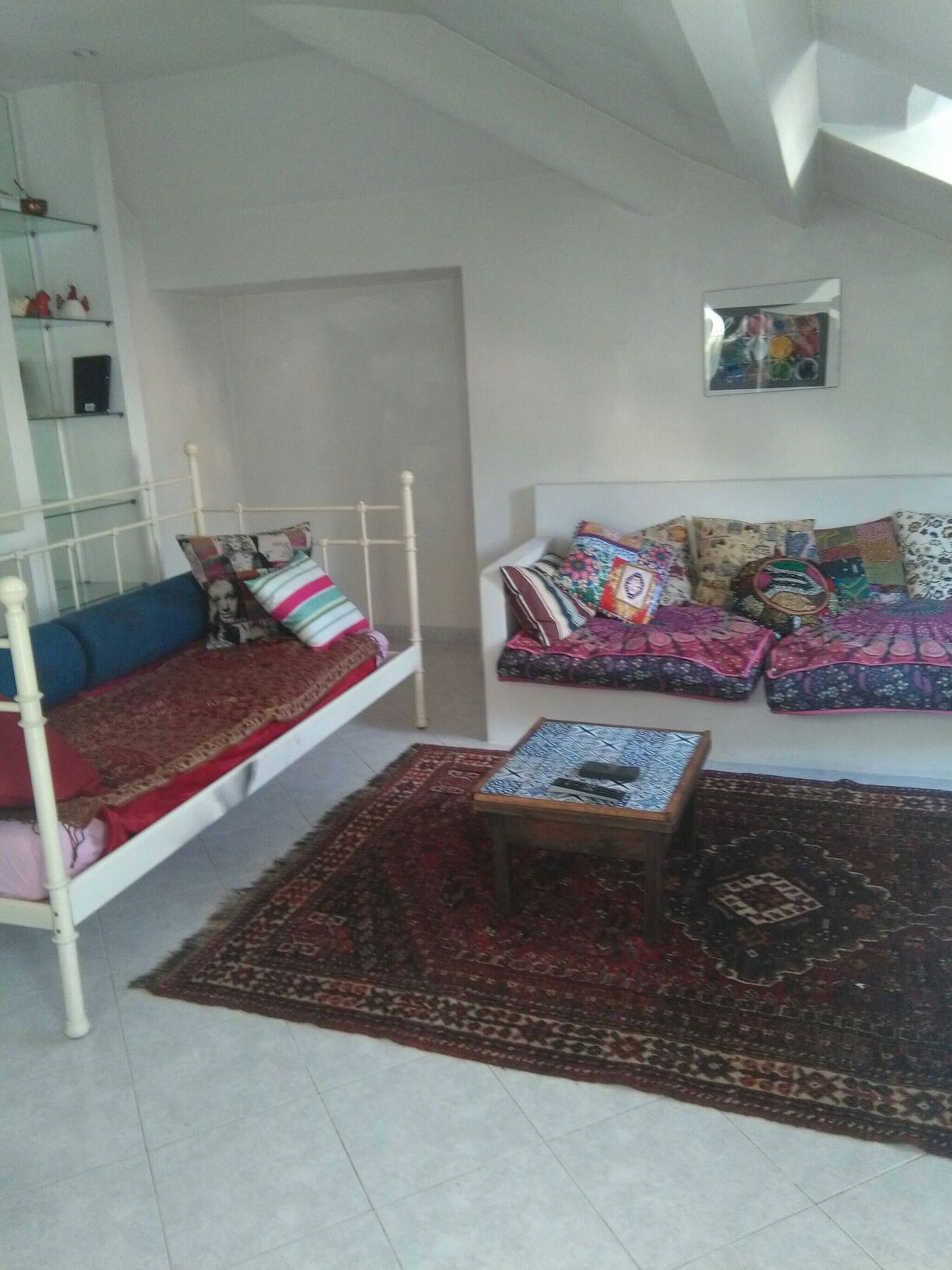 A room with a bed, a sofa, a coffee table, and a patterned rug.