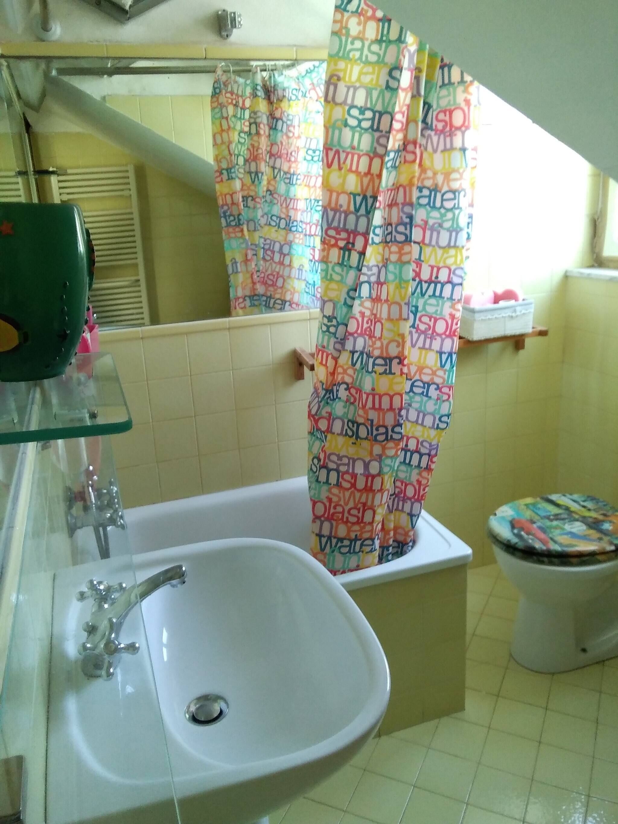 Een badkamer met een witte wastafel, een douchegordijn met kleurrijke tekst en een toilet met een decoratieve zitting.