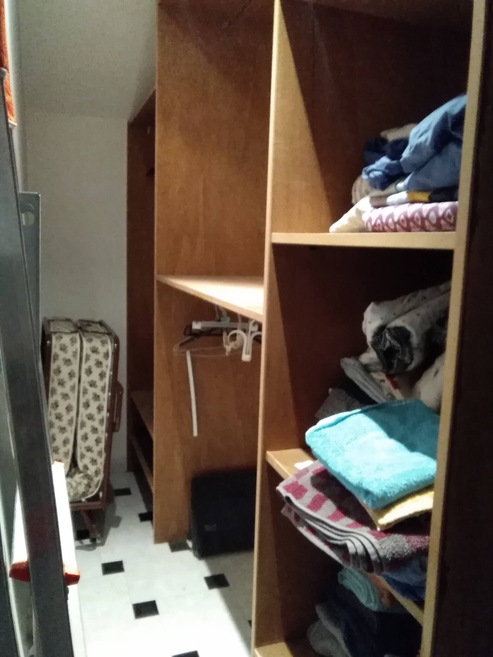A narrow hallway with a wooden wardrobe, a patterned suitcase, and a tiled floor.