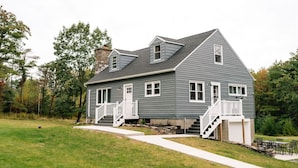 A two-story house with a stone chimney, white railings, and a front porch. - Modern Country Farmhouse, Walking Distance to Lake (Averill Park)