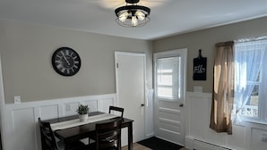 A dining area with a wooden table, chairs, a wall clock, and a ceiling light fixture. - Modern Country Farmhouse, Walking Distance to Lake (Averill Park)
