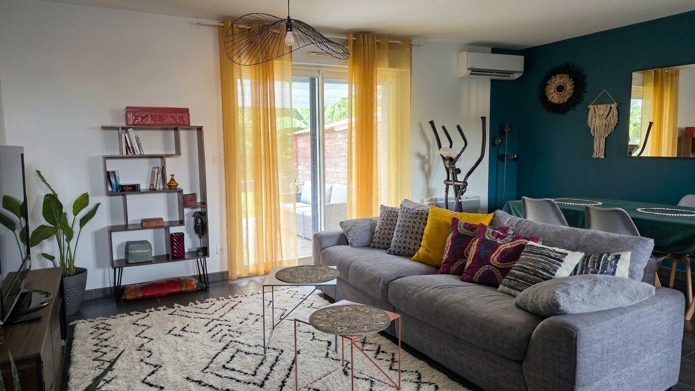 Un salon moderne avec un canapé gris, des coussins à motifs, un tapis blanc et une bibliothèque.