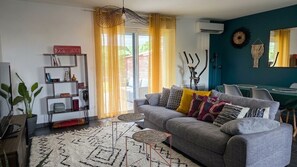 Un salon moderne avec un canapé gris, des coussins à motifs, un tapis blanc et une bibliothèque.