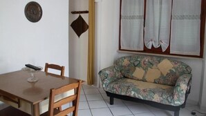 A dining area with a wooden table and chairs, a sofa with floral upholstery, and a window with curtains. - Casa Miclara apartment -- Agave (Zanca)