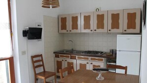 A compact kitchen with white cabinets, a stove, a sink, and a dining table with chairs. - Casa Miclara apartment -- Agave (Zanca)