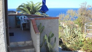 A patio with a white chair and a blue umbrella, overlooking a coastal view with cacti and a clear sky. - Casa Miclara apartment -- Agave (Zanca)