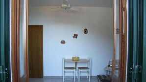 A room with a wooden door, a white ceiling fan, a small table with two chairs, and a bed with a plaid blanket. - House Miclara studio apartment -- Almond tree (Zanca)