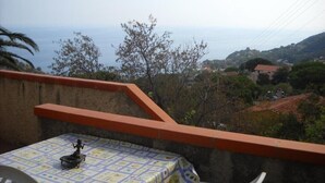 A balcony with a table, a statue, and a view of the sea and distant buildings. - House Miclara studio apartment -- Almond tree (Zanca)