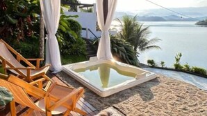A deck with wooden chairs and a hot tub overlooking a body of water. - Oasis Beach House (Angra dos Reis)