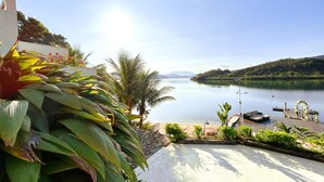 A lakeside view with a dock, boats, and lush greenery. - Oasis Beach House (Angra dos Reis)