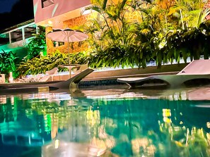 A swimming pool with a reflection of palm trees and a building with a stone facade. - Oasis Beach House (Angra dos Reis)