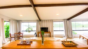 A spacious room with a large window, a wooden bar area, and a television. - Oasis Beach House (Angra dos Reis)