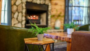 Un interior acogedor con una chimenea de piedra, un banco acolchado verde y una pequeña mesa de madera con una planta en maceta.