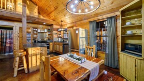 Interior de una cabaña de madera con comedor, cocina y estanterías empotradas.