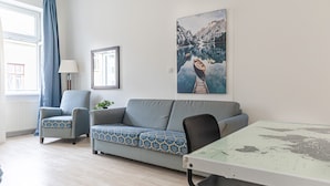 Ein modernes Wohnzimmer mit einer Couch, Sesseln, einem Glastisch und einem Gemälde einer Bergseenlandschaft.