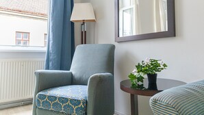 Ein Zimmer mit blauem Sessel, einem kleinen runden Tisch mit Topfpflanze, einer Stehlampe und einem großen Spiegel an der Wand.
