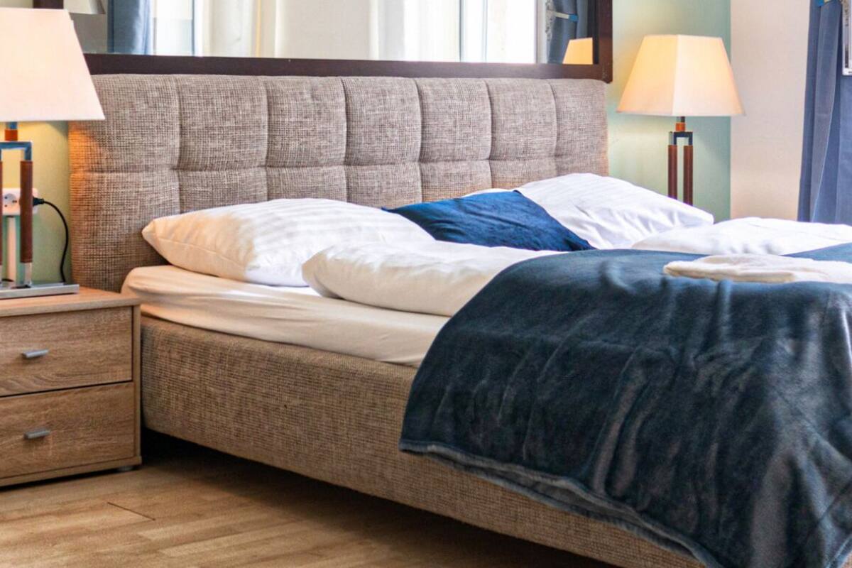 A neatly made bed with a blue blanket, two bedside lamps, and a wooden nightstand with drawers.