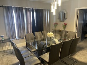 Un coin repas avec une table et des chaises en verre, un miroir au mur et une fenêtre avec des rideaux.