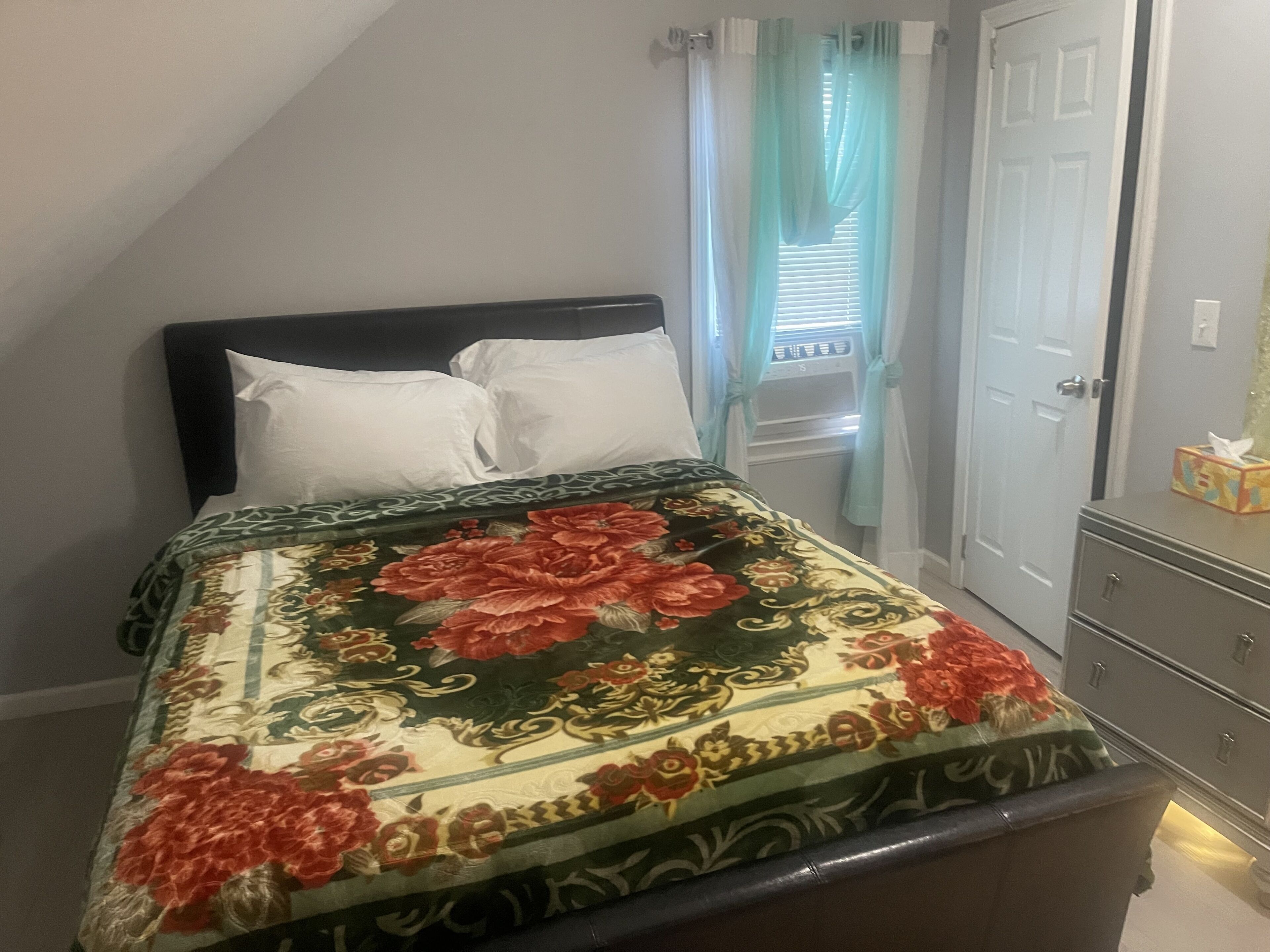 Une chambre à coucher avec un lit, une commode, une fenêtre avec des rideaux et une porte.