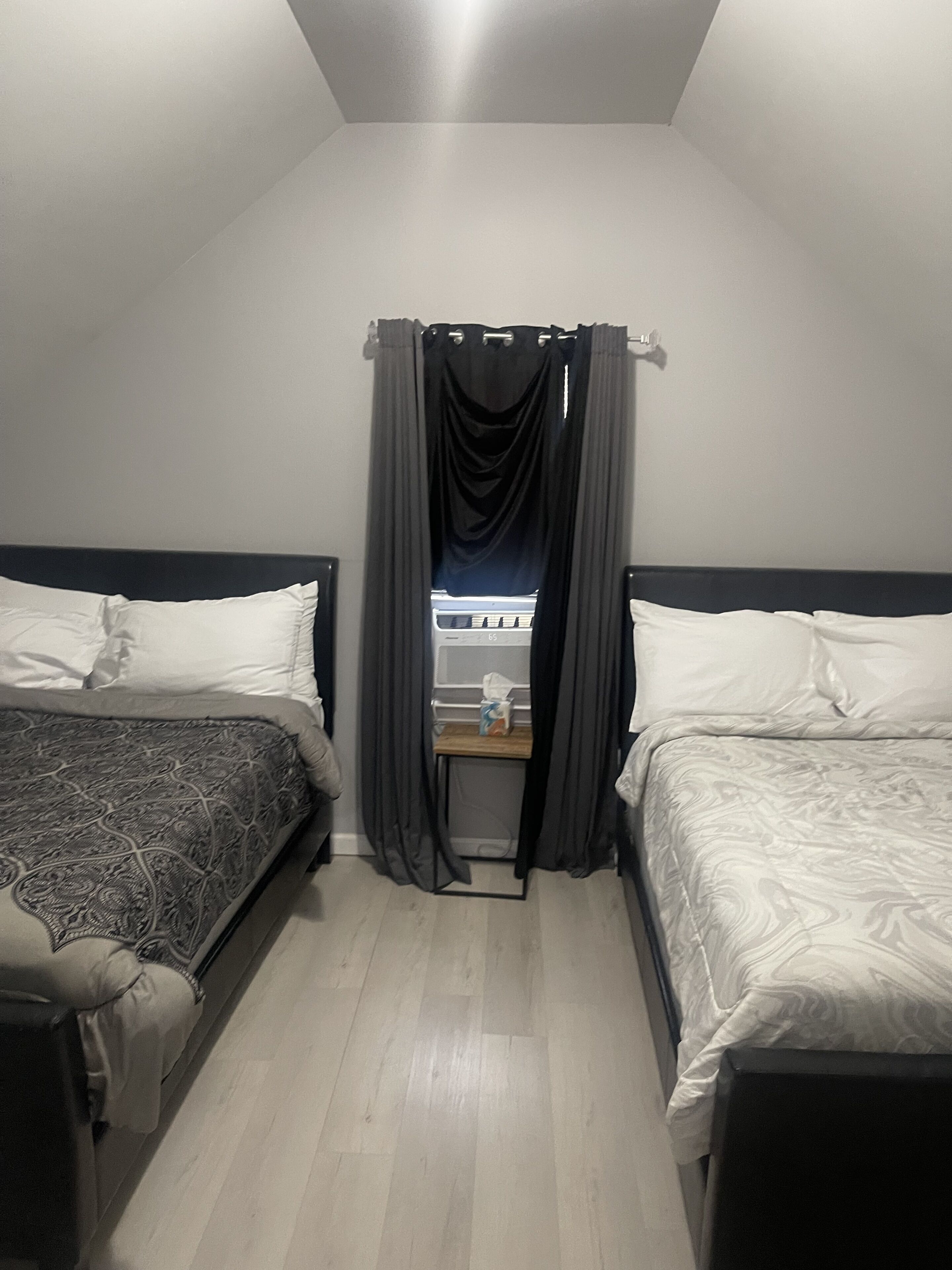 A bedroom with two beds, a small table, and a window with curtains.
