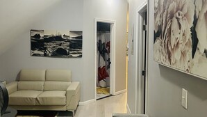 Un salon avec un canapé beige, un fauteuil gris, un ventilateur et un grand tableau floral accroché au mur.