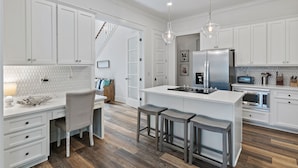 A modern kitchen with white cabinetry, a central island with stools, a stainless steel refrigerator, and a microwave.
