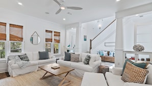 A spacious living room with a white sofa set, a wooden coffee table, and a ceiling fan.