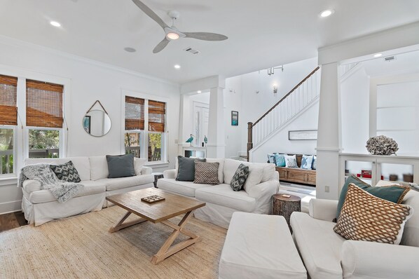 A spacious living room with a white sofa set, a wooden coffee table, and a ceiling fan.