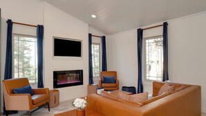 Un salon moderne comprenant un canapé, deux fauteuils, une table basse, un téléviseur à écran plat et une cheminée.