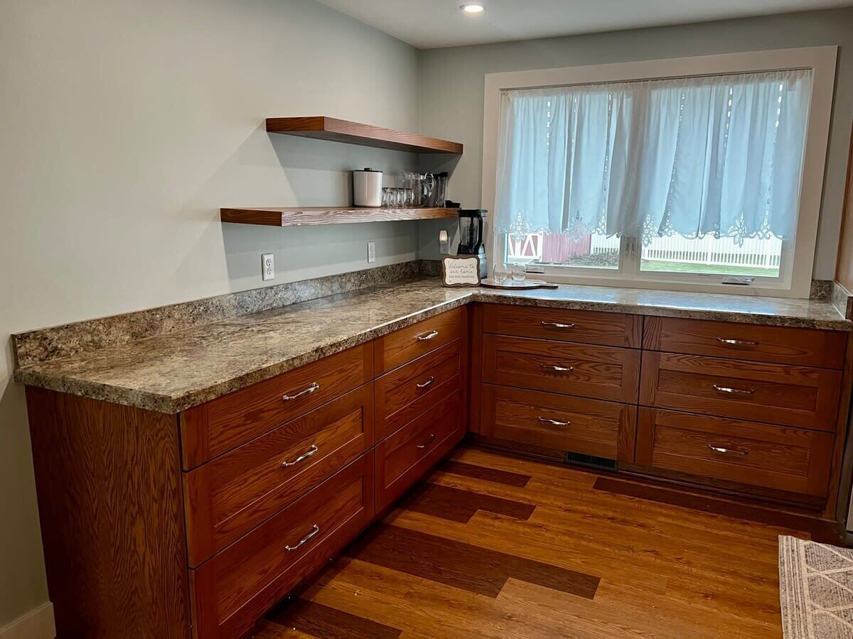 A kitchen with wooden cabinets, granite countertops, and a window with sheer curtains.